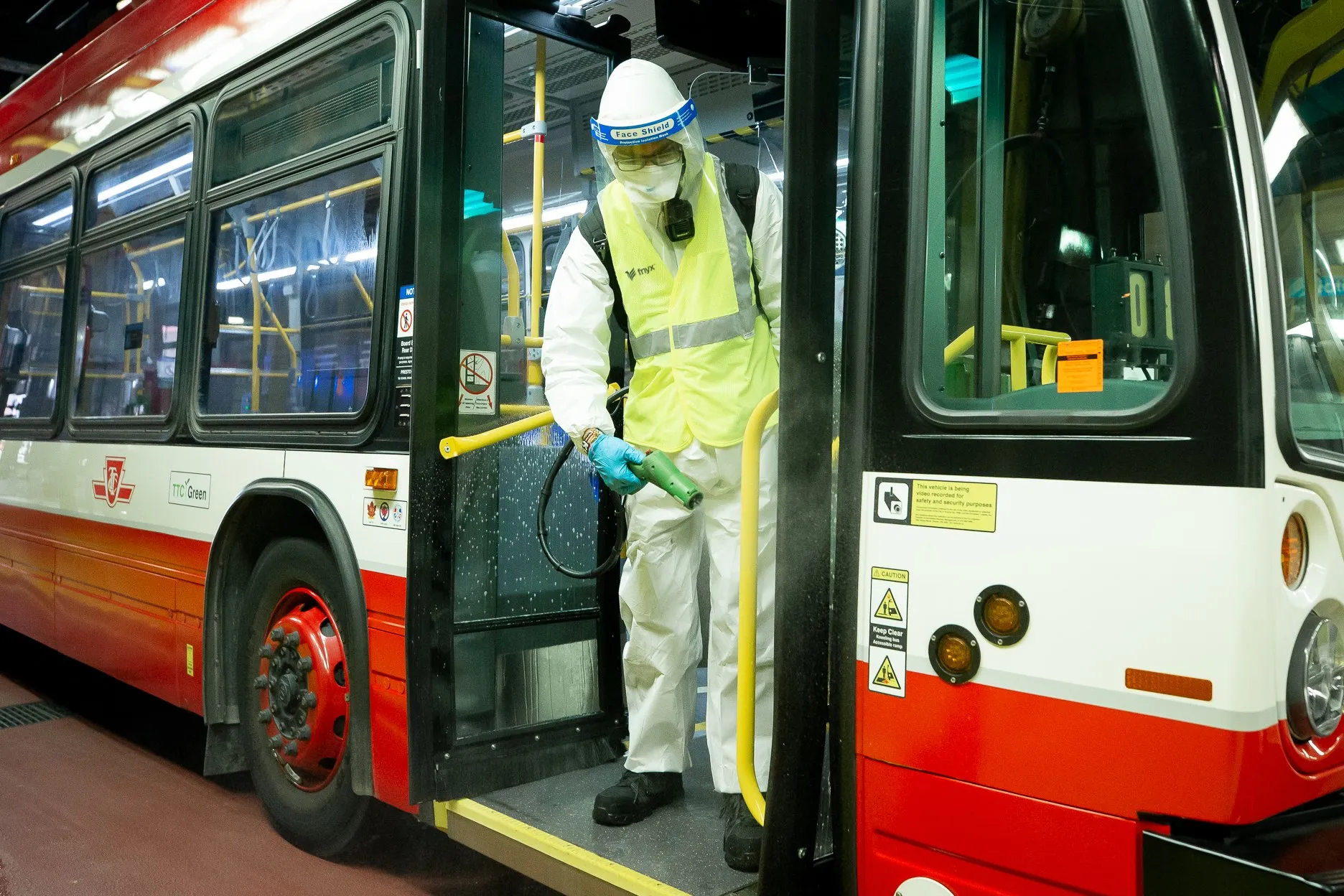 A Fnyx team member in protective equipment disinfecting the entrance of a TTC bus